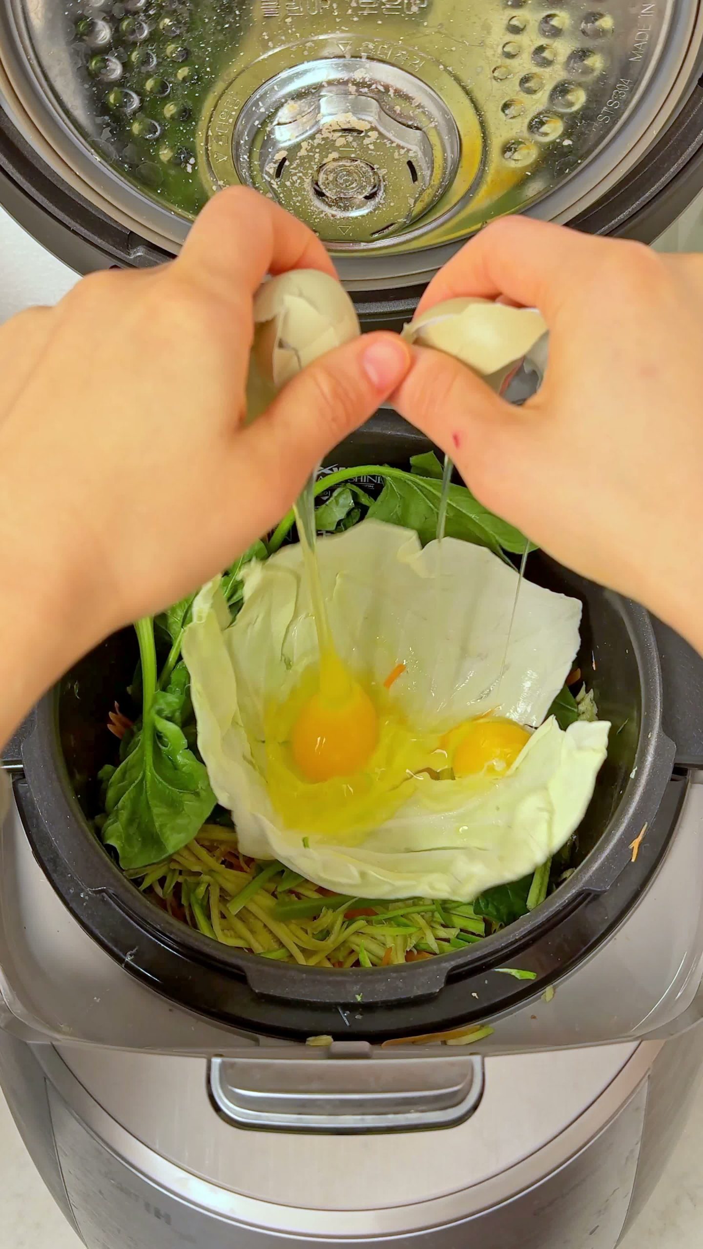 Cracking eggs on top of the bibimbap vegetables in the rice cooker