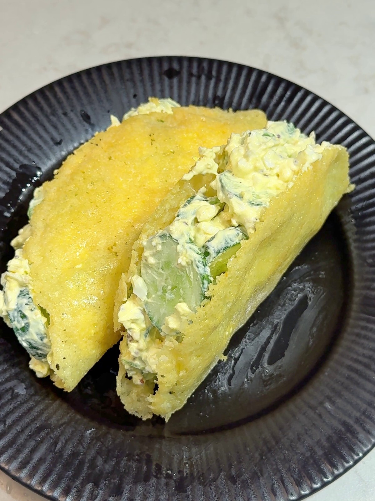 Cheese taco shell folded around an egg and cucumber filling