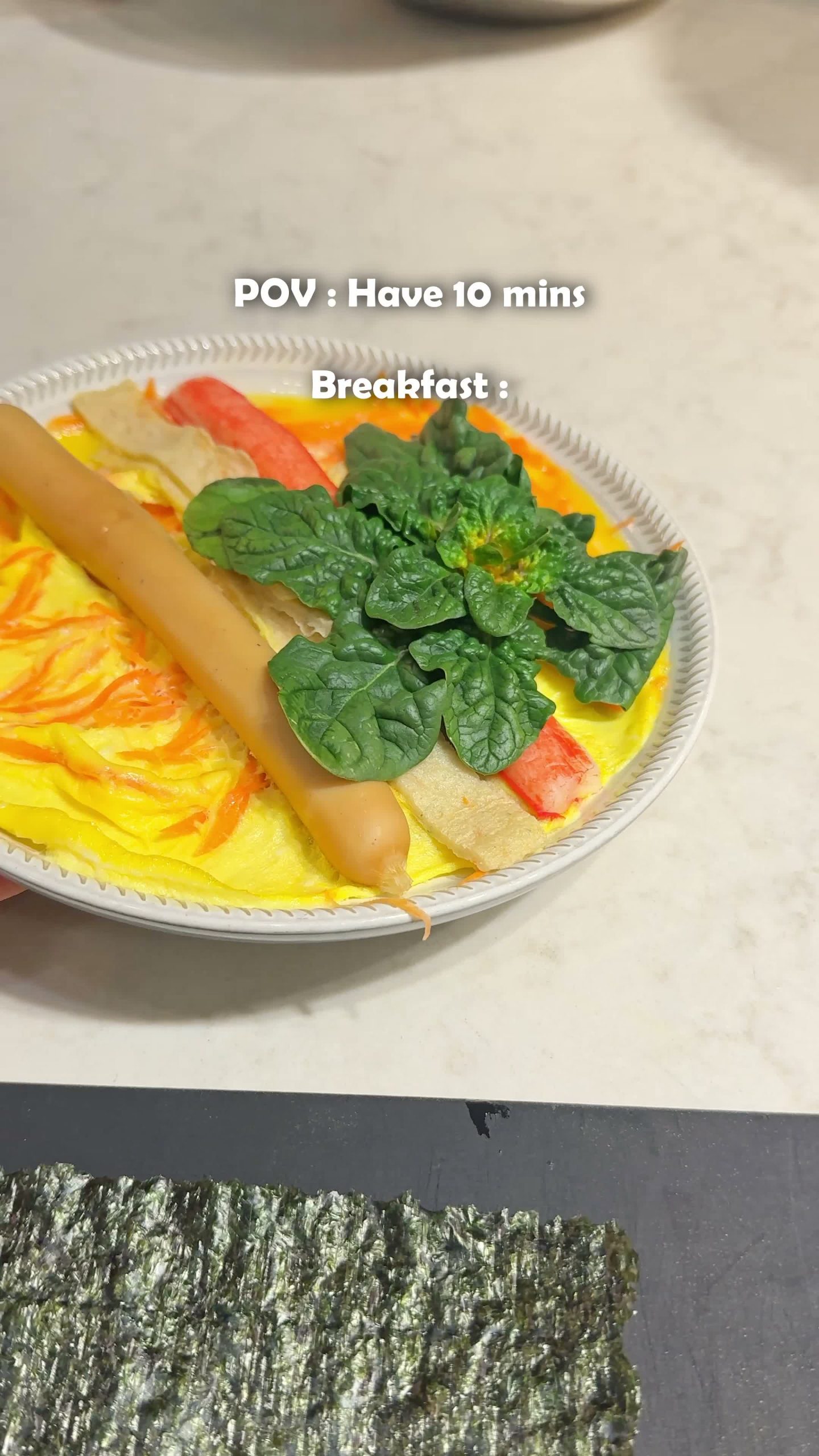 Cooked egg sheet topped with carrot, crab stick, and spinach, ready to roll