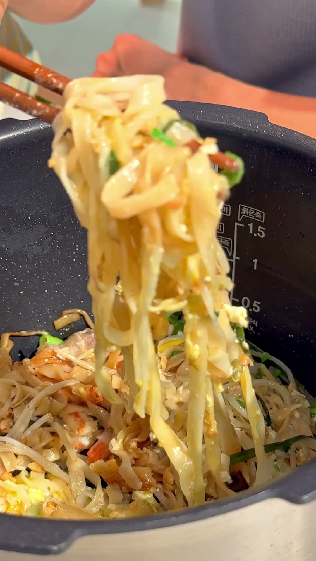 Chopsticks lifting a tangle of finished pad thai noodles from the pot