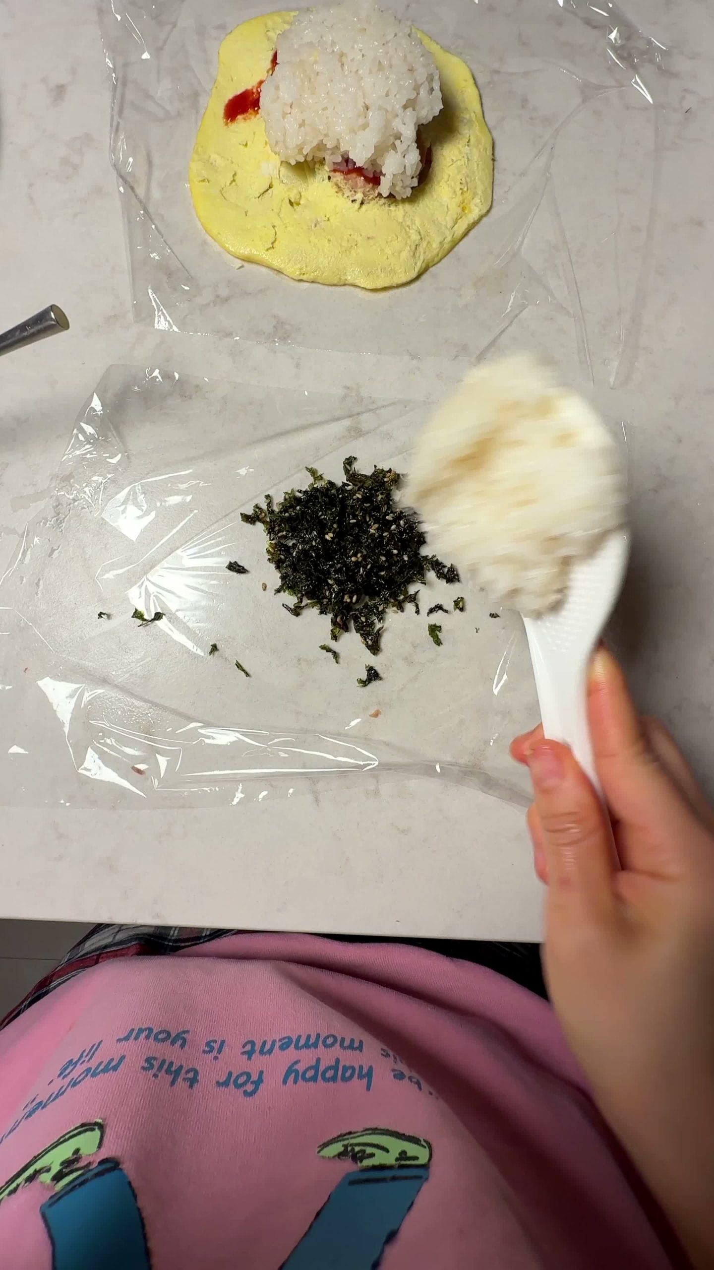 Seasoned seaweed flakes sprinkled over rice on plastic wrap