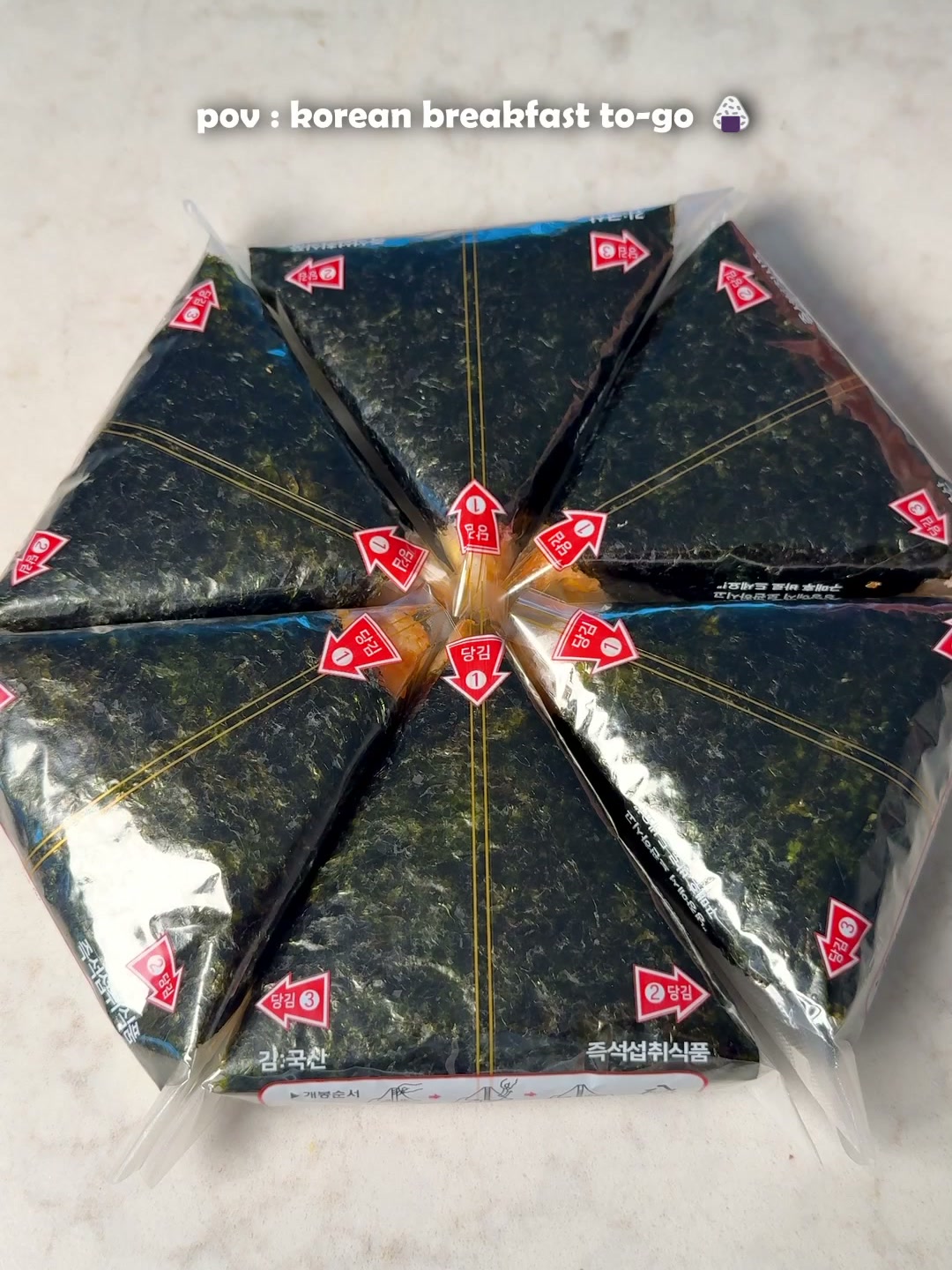 Six samgak gimbap, each individually wrapped in seaweed packaging, arranged in a flower pattern