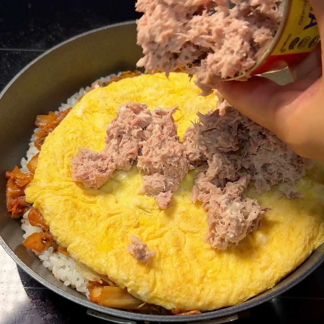 Tuna mayo being scattered over the egg sheet layer in the pan