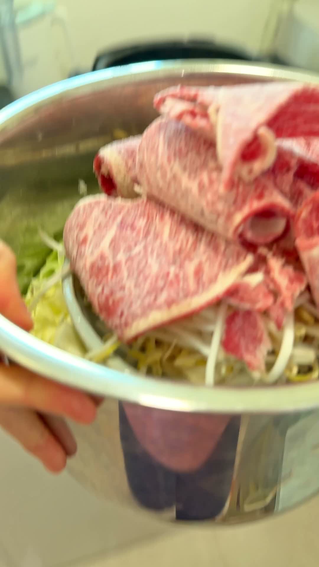 Thinly sliced shabu-shabu beef draped over enoki mushrooms and bean sprouts in the pot