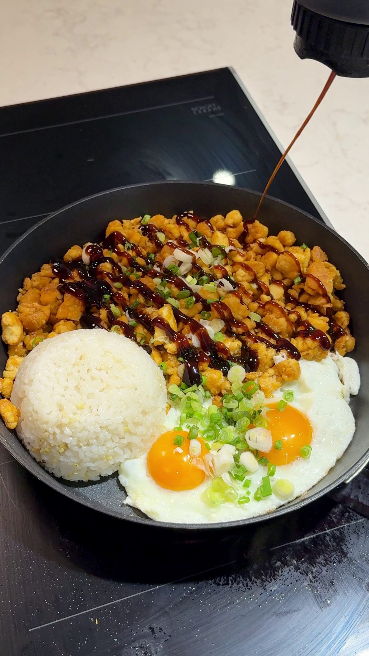 Tofu crumble rice bowl drizzled with teriyaki sauce next to sunny-side-up eggs