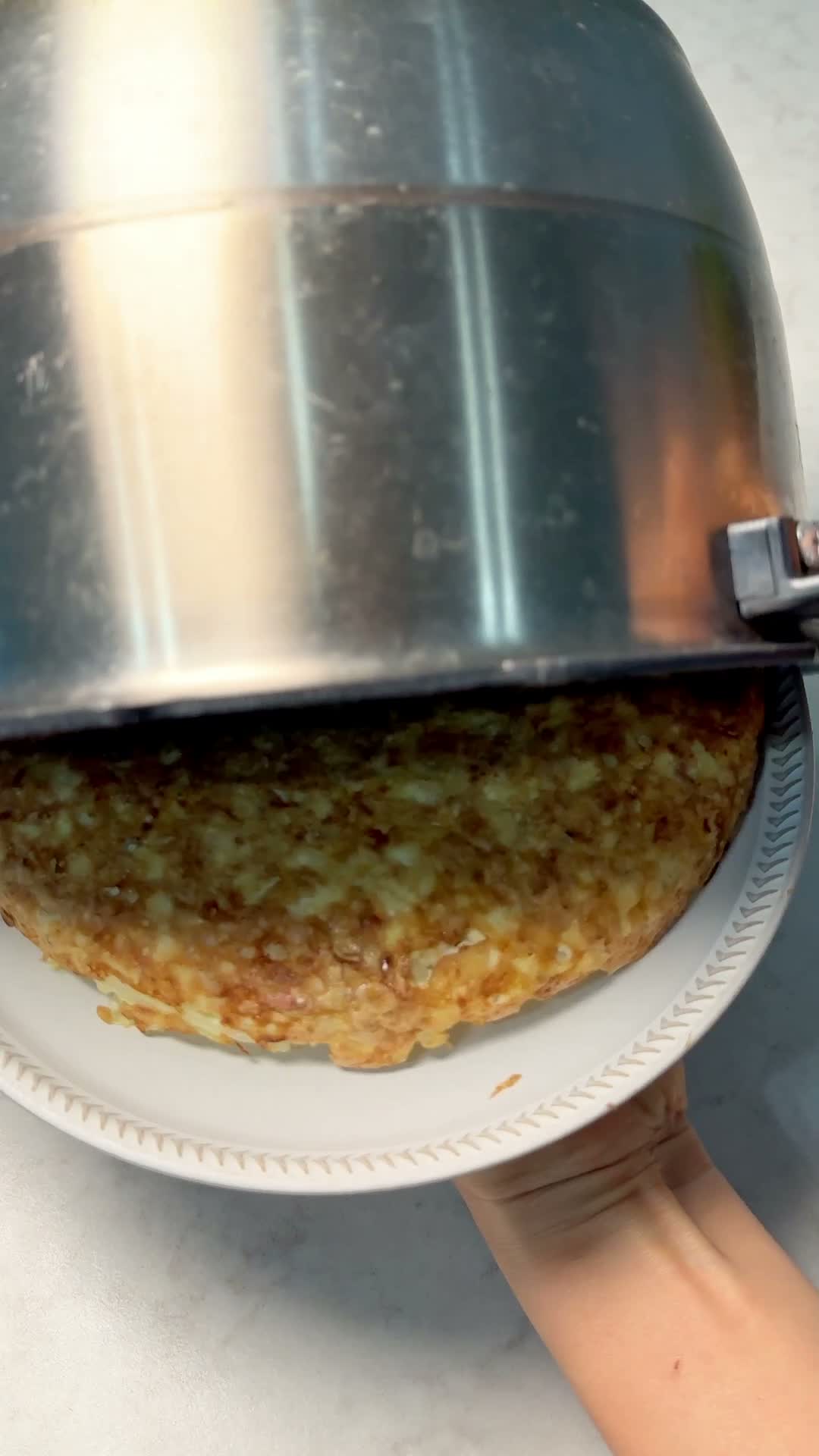 Lifting the rice cooker pot off to reveal the golden tofu okonomiyaki pancake on a plate