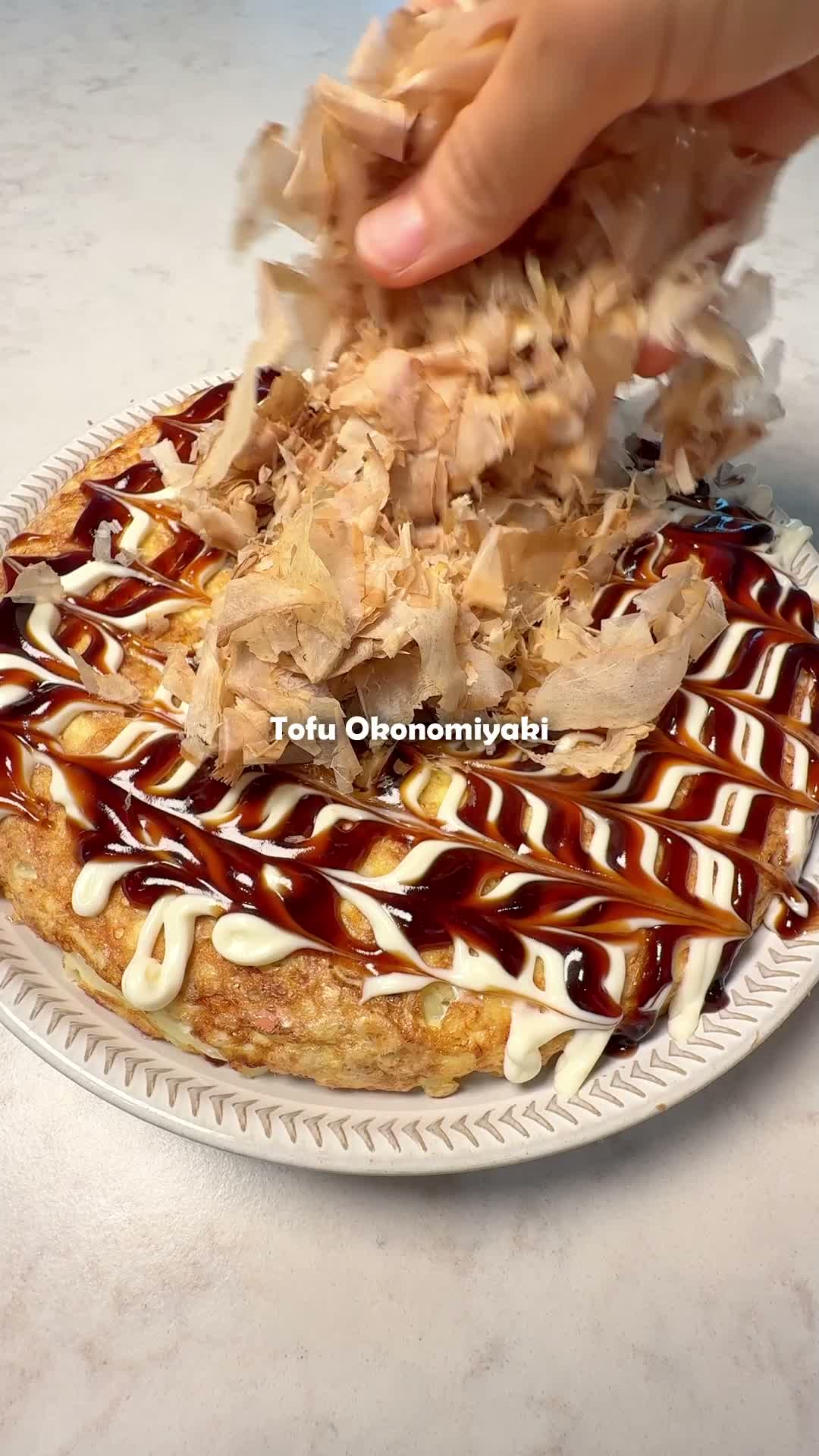 Sprinkling a handful of bonito flakes over the sauced tofu okonomiyaki